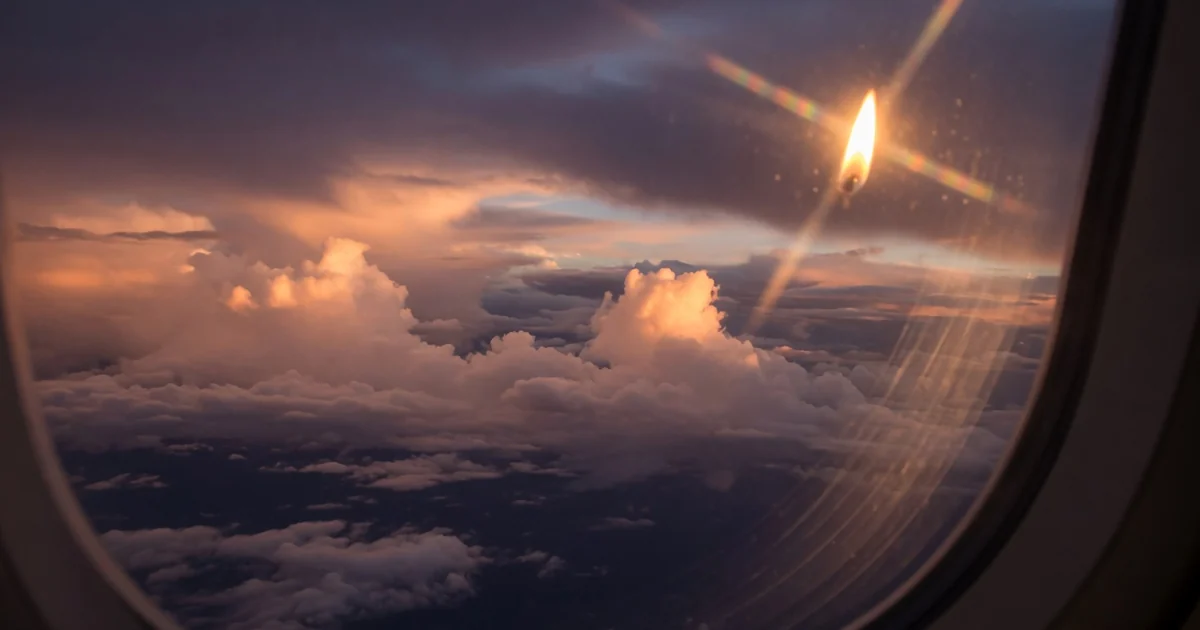 Vedere prin fereastra avionului peste nori la apus auriu